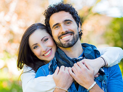 A man and a woman smiling together, with the man standing behind the woman.